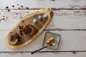 תמונה עיצובית. משטח עץ ועליו מונחים קינוחים. כדורי שוקולד, מוס שוקולד ובוואריה עם סירופ שוקולד