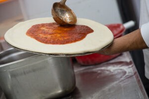 יוצקים רוטב עגבניות על בצק הפיצה בצורה מעגלית.